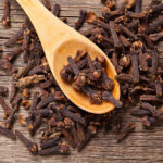 Closeup of cloves in wooden teaspoon on wooden background; Adobe RGB color space;