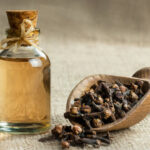 Close up glass bottle of clove oil and cloves in wooden shovel on burlap sack. Essential oil of clove rustic style background spice concept